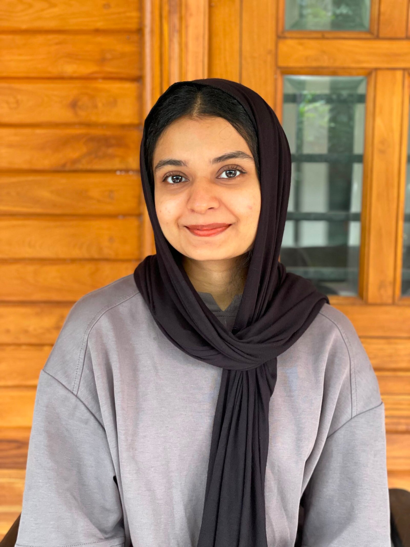 Best digital marketing freelancer in Calicut, Amina Ladheedha, smiling in a professional portrait wearing a black hijab and grey top.